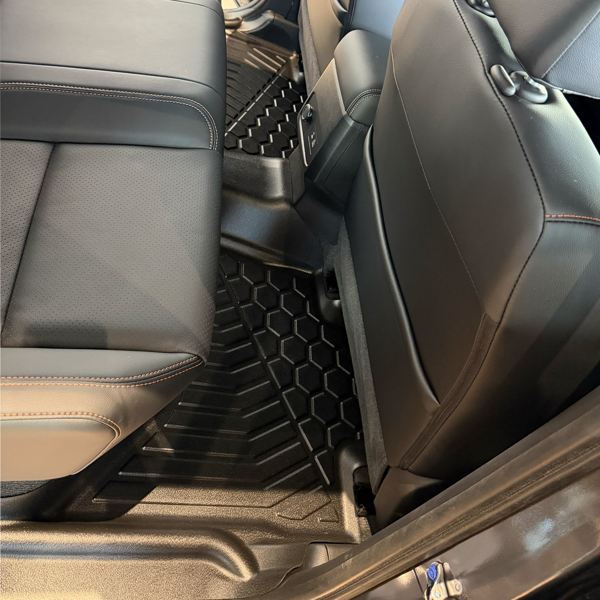Black TPE floor mats installed in the rear of a vehicle, shown between grey seats.